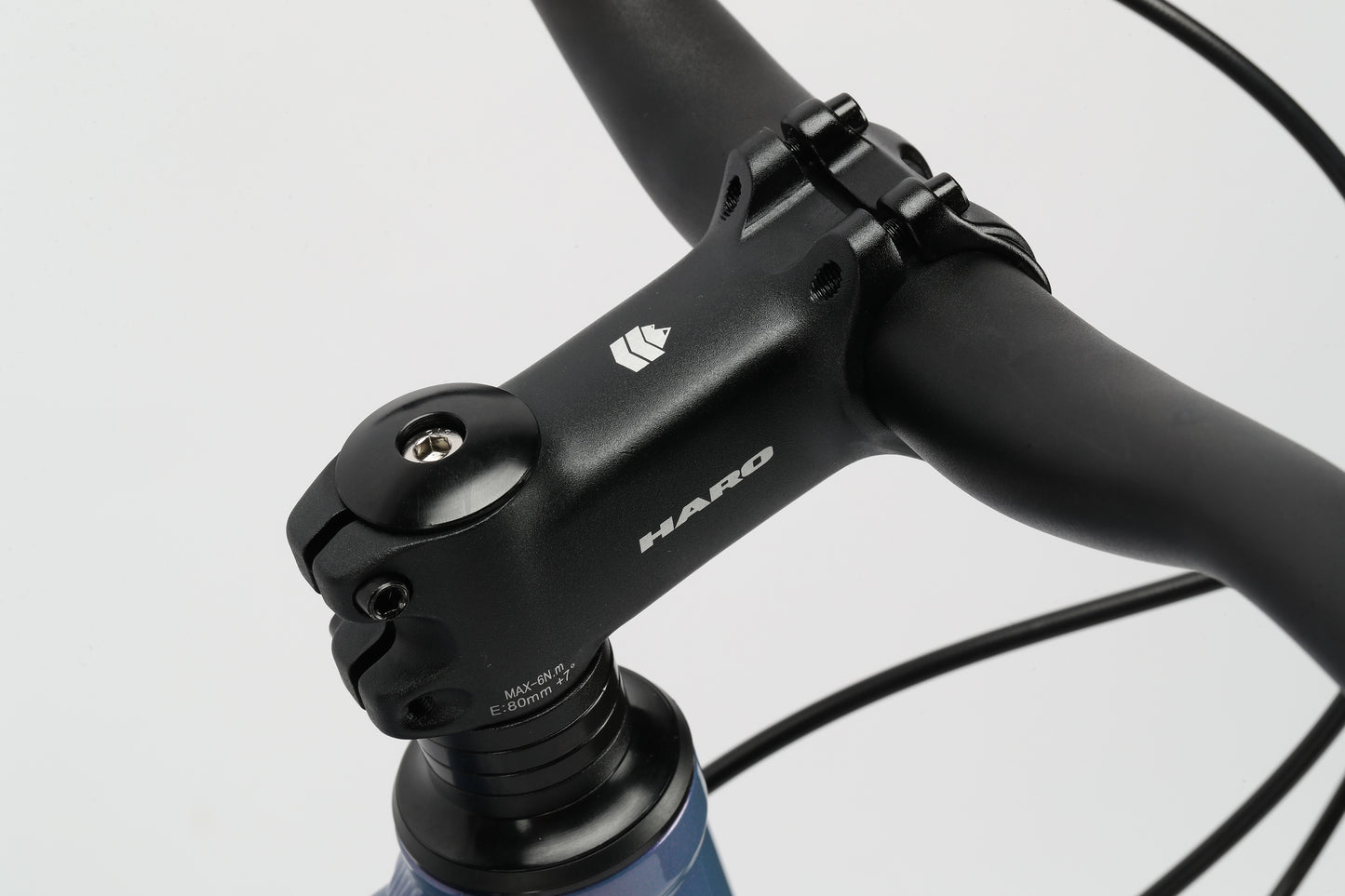 Close-up of a handlebar and stem branded with Haro MTB Beasley 27.5 DLX. The black stem smoothly joins the blue aluminum frame, highlighting the clean design and assembly of the bikes front components.