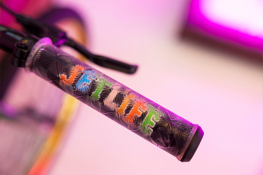 Close-up of a Jetlife x CEEK 29” bicycle handlebar grip with an abstract pattern and smile visible. The blurred background of bright pink and purple evokes the vibrant spirit of a Haro Bikes ride.