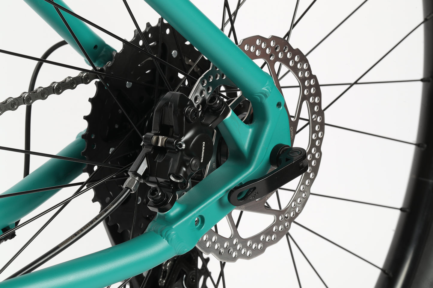 Close-up of Flightline LTD 29s teal rear disc brake, Shimano Cues cassette, and chain on a white background.