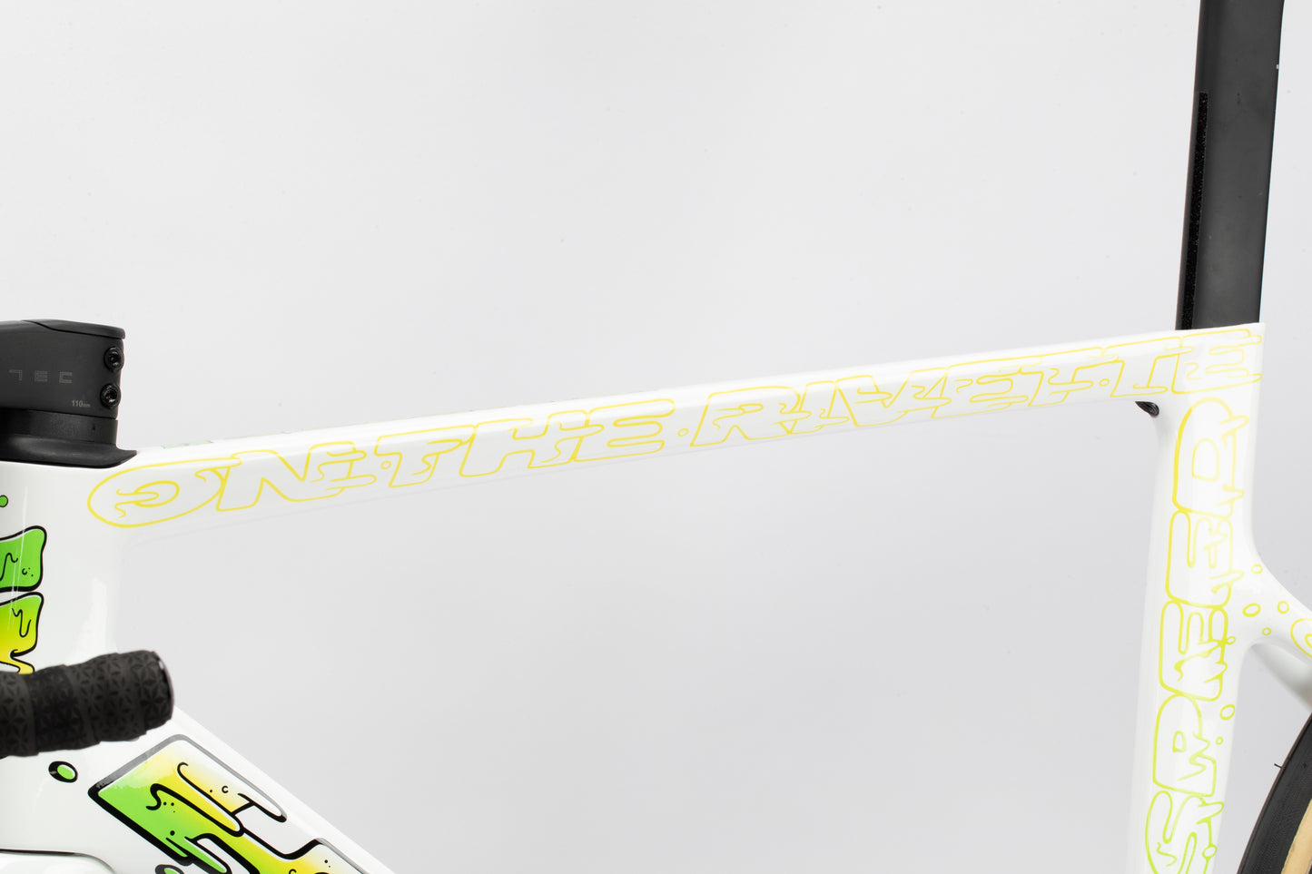 Close-up of a Rivette Carbon LTD frame with ON THE RIVET in yellow, set against abstract green patterns on white.