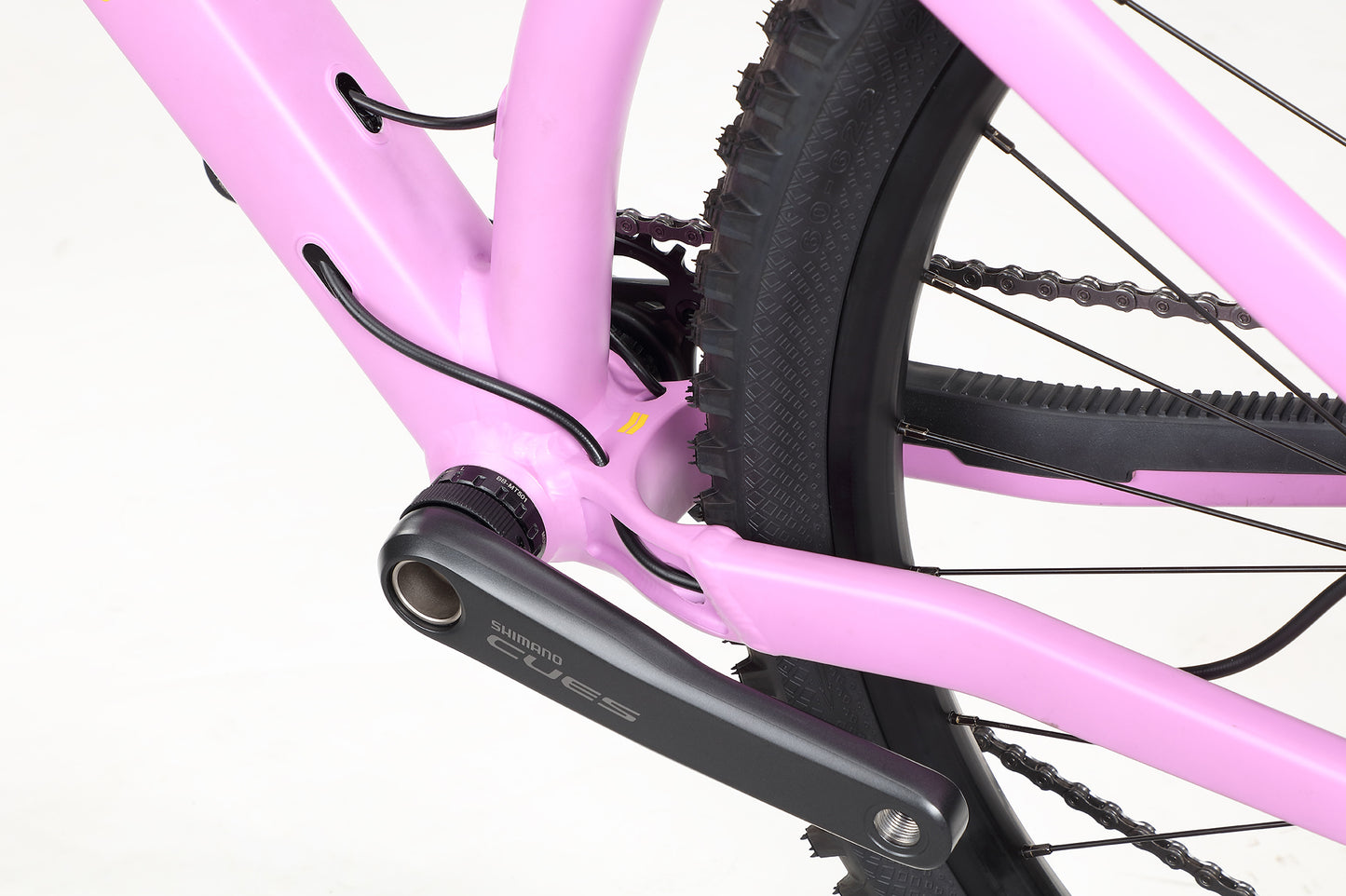Close-up of the Saguaro 3 by Haro MTB: Featuring a pink aluminum frame with a Shimano crankset at the rear, visible wiring, a black tire, and part of the chain showcasing its aggressive geometry.