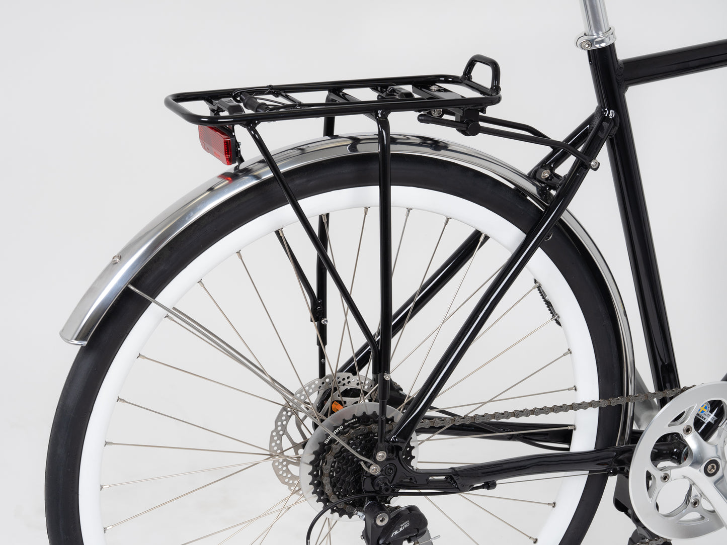 A close-up of a bicycles rear wheel highlights the gear system with an Atran Velo City AM Rear Carrier integrated into the black metal luggage rack. The white tire with a silver rim and rear mudguard enhance the black frame, set against a plain white background.
