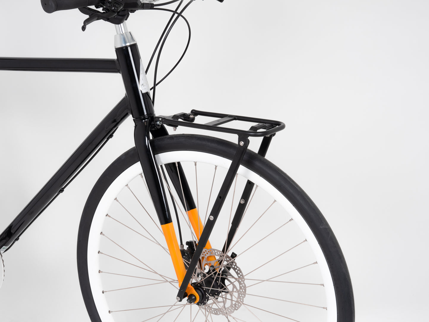 Close-up of the Atran Velo Hybrid AM Front Carrier in black with an orange accent, made from lightweight aluminum. It includes a front cargo rack above a disc brake and white-rimmed wheel, set against a plain white background.