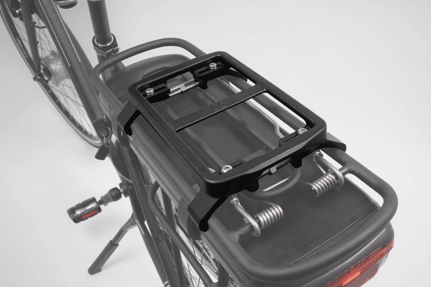 A rear view of the bicycle highlights the NEWRACK UNI AVS Adapter by Atran Velo, a black metal rack designed for AVS bags, attached above the back wheel. The bike also features a taillight and is set against a neutral background.