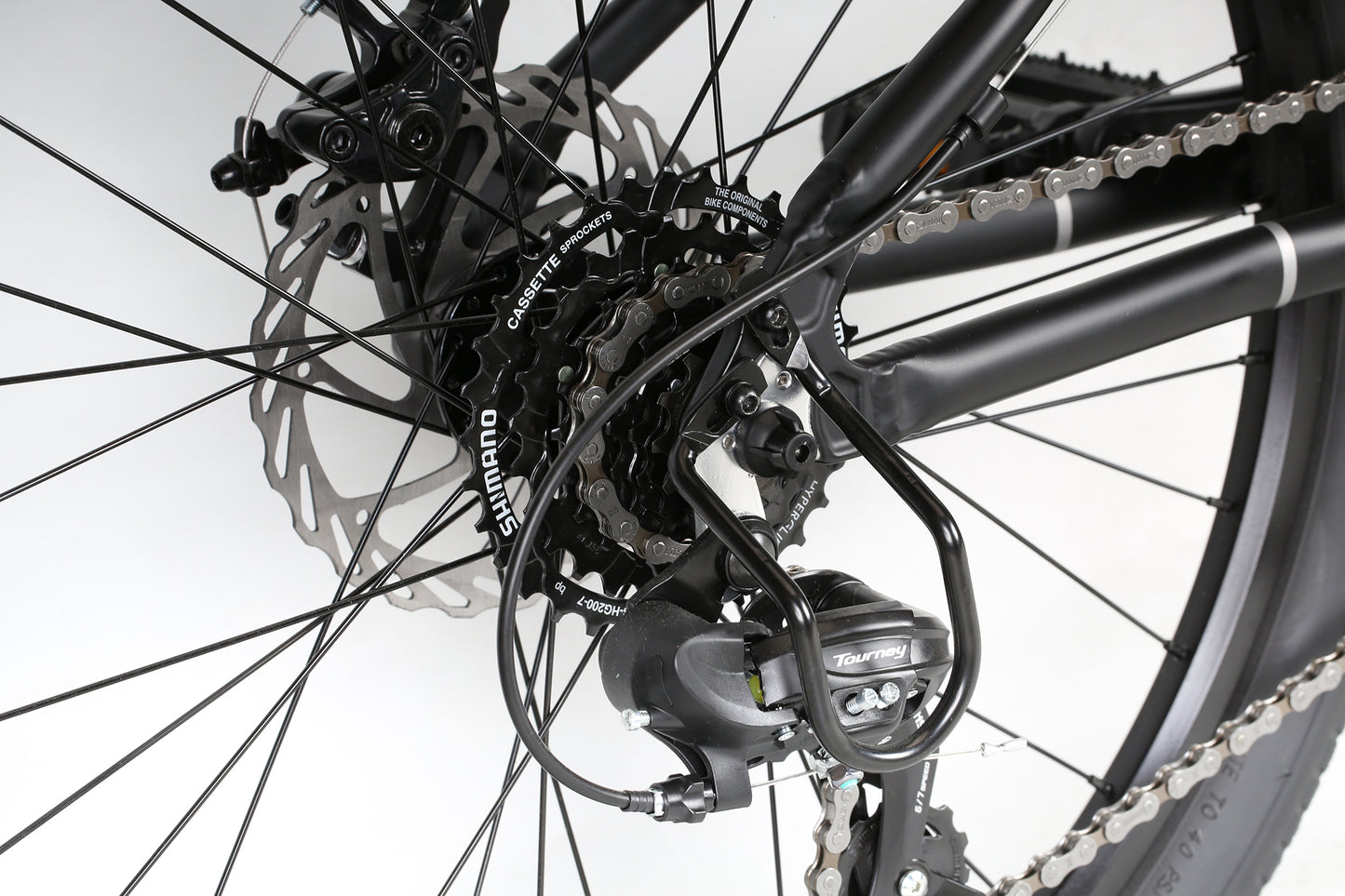 A close-up of the Beasley 24 by Haro MTB shows the rear derailleur and gear cassette with black Shimano components, including the Revo Shifter, visible. The chain wraps around the gears as spokes and part of the tire are also in view.