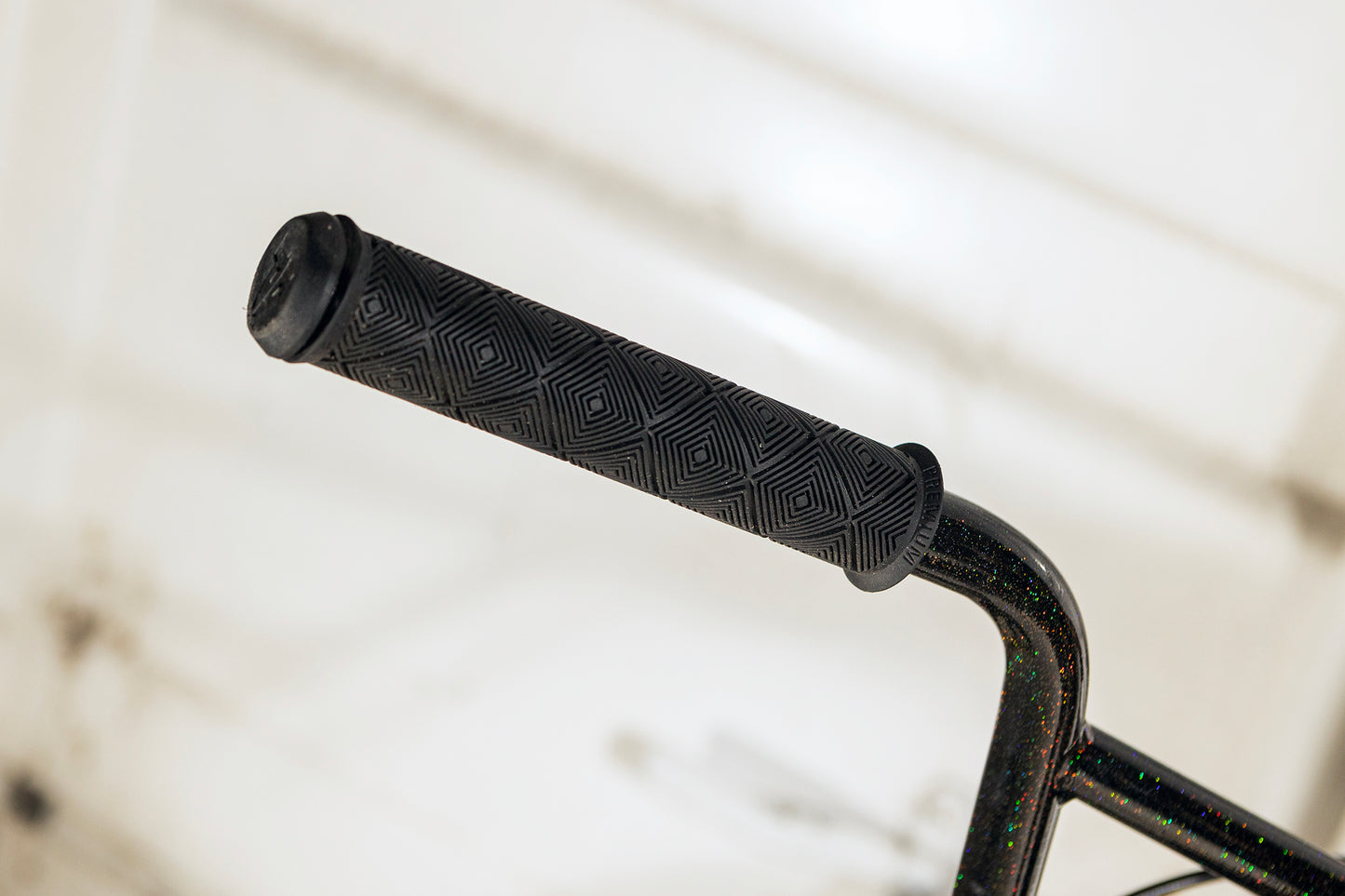 Close-up of the B.M.F 26 BMX handlebar by Haro Bikes, featuring a geometric textured black grip. The reflective design embodies Bike Life, with a blurred background highlighting the grips details—a tribute to Chad Kerleys style.