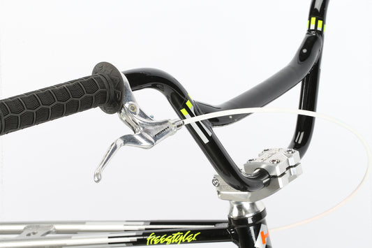 Close-up of the DMC 26 BMX: black handlebar, V-brakes, yellow grip accents, and “freestyle” on its aluminum frame.