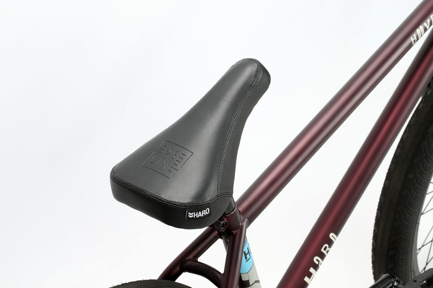 Close-up of a black bicycle seat with the Haro Bikes logo on it, attached to a maroon chromoly Hoover bike frame, set against a plain white background.