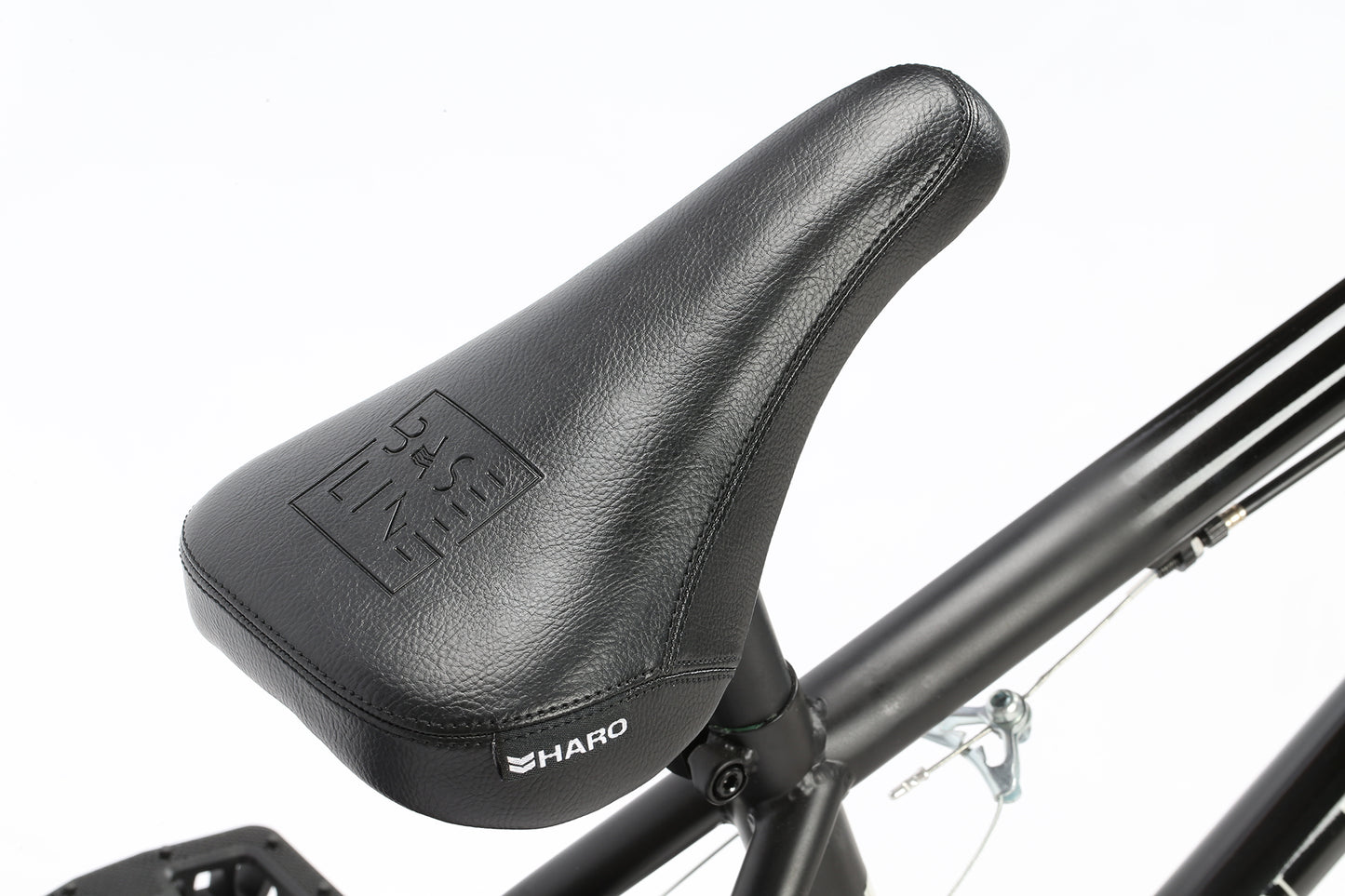 A close-up of the Interstate Matte Black/Gloss Black bicycle seat shows Haro Bikes and BASE LINE embossed on it. This BMX bike boasts a sleek chromoly frame and sealed bearings, all set against a pristine white backdrop.
