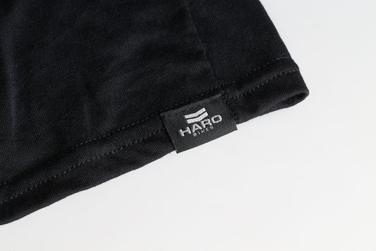Close-up of a black fabric label reading Haro Bikes in white text, showcasing DryBlend technology. The label is sewn onto a black Haro MTB DryBlend Shirt with visible stitching around the edges. The pre-shrunk jersey fabric looks soft and smooth.
