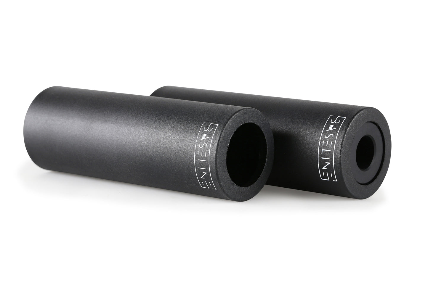 Two cylindrical objects rest on a white background, each with a smooth surface and BASELIN3 in white lettering. They hint at precision and durability, evoking the grace of a tool that grinds effortlessly. Product: Baseline Plastic Peg. Brand: Haro Bikes.