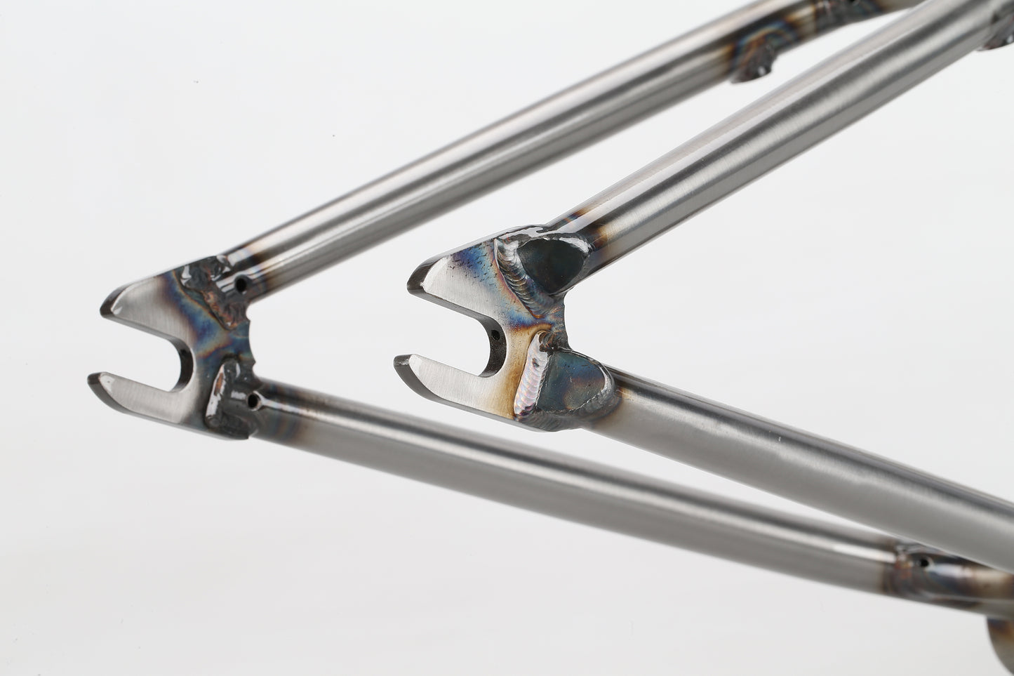 A close-up of the Haro Bikes SD V3 Frame reveals intricate welding and joints. The metallic surfaces have a rainbow-like discoloration from heat treatment, set against a soft white background to highlight the craftsmanship Dennis Enarson relies on for his versatile BMX rides.