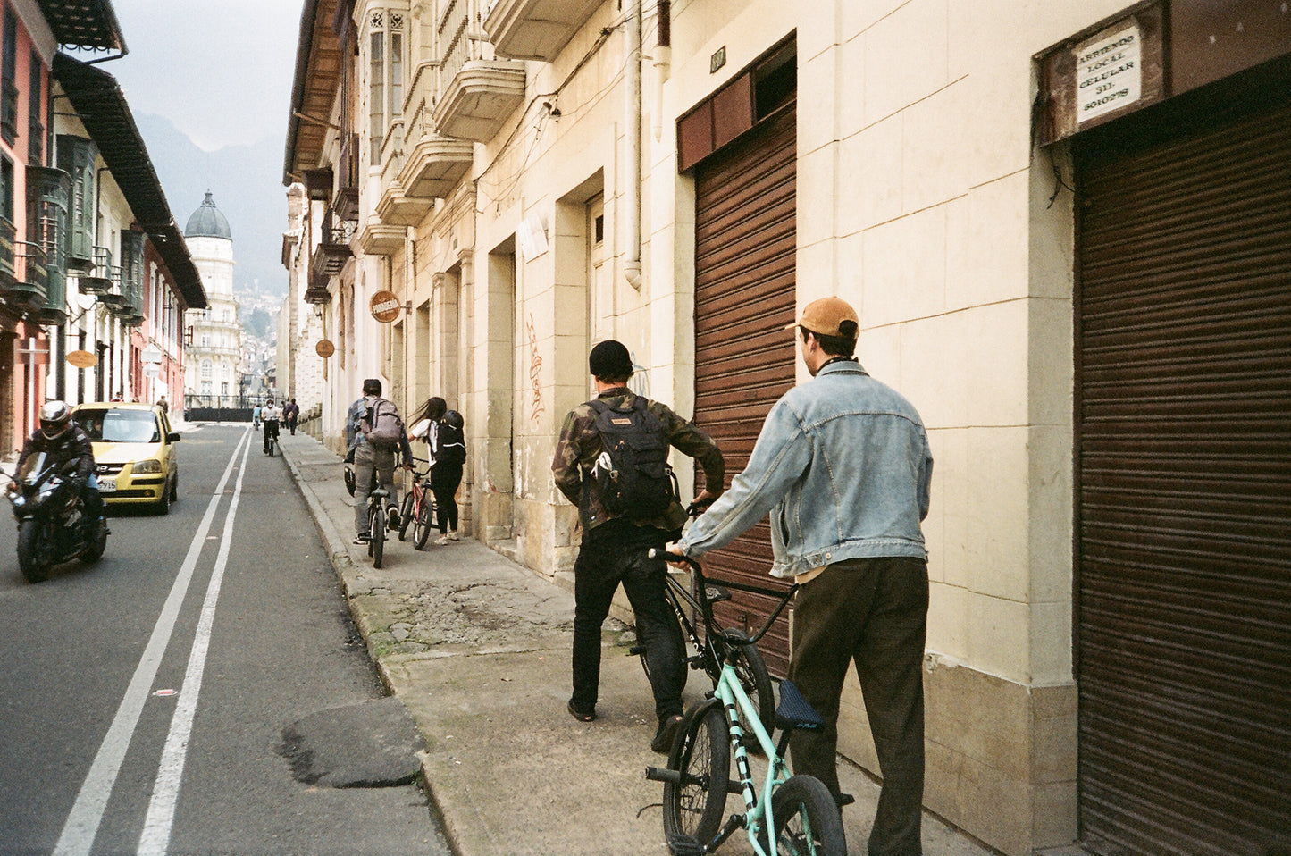 People with bicycles walk a narrow city street, perfect for cruising or showing off tricks on the La Bastille Freecoaster.
