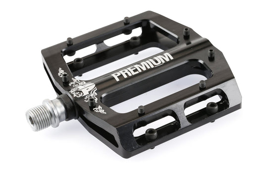 A close-up of Premiums Slim Pedals shows a black pedal with an ultra-thin profile, metal spindle, small protruding pins for traction, and cutouts for reduced weight. PREMIUM is printed in white on the surface.