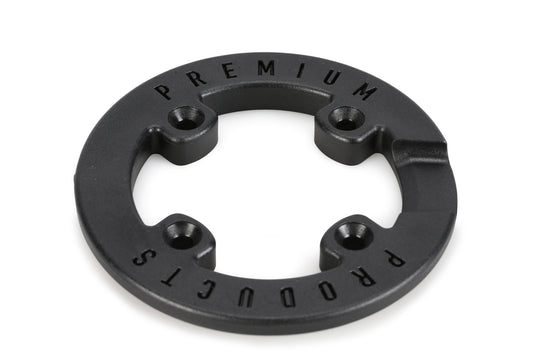 The Premium Sprocket Guard by Premium is a circular black metal object featuring four evenly spaced holes and raised text PREMIUM PRODUCTS around its edge, shown against a white background.