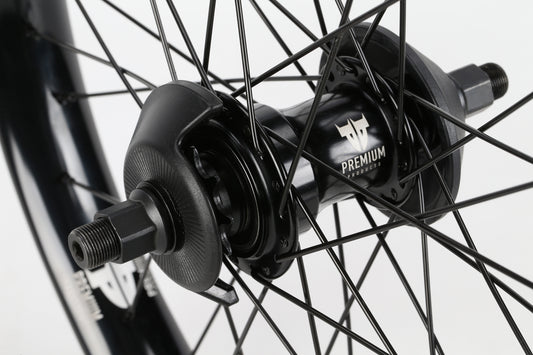 Close-up of a black wheel hub from the Premium brand, with Premium and a logo on it. The intricately laced hub connects to a shiny rim, displaying craftsmanship similar to that of the Curb Cutter Freecoaster Rear Wheel.
