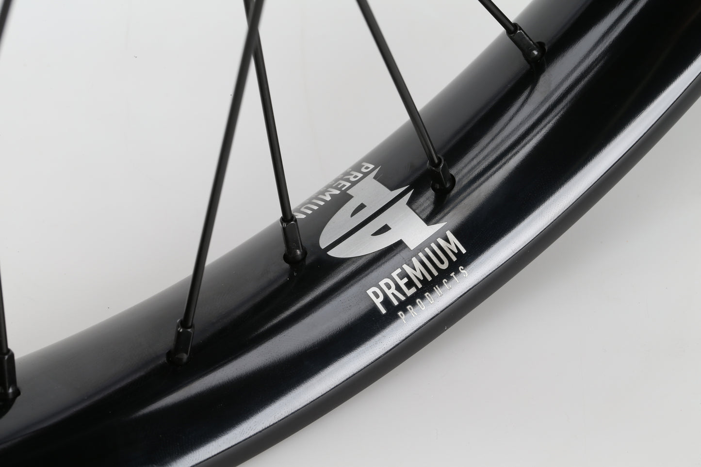 Close-up of a black bicycle wheel with a silver P logo and the word PREMIUM, featuring the Curb Cutter Freecoaster Rear Wheel. Thin black spokes extend from a freecoaster hub, set against a light gray background.