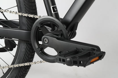 Close-up of a Haro MTB PD1 27.5 police bikes black pedal and crankset with chain, rear wheel, and textured tire. The pedal includes a reflective strip, enhancing the stealthy look of its sleek, dark frame.