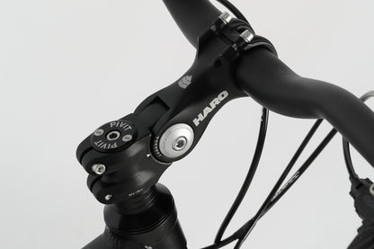 Close-up of a PD2 27.5 bicycles handlebar and stem. The black stem, featuring Haro MTB markings, connects to a tapered head tube. Black cables run along the frame with a minimalist design against a light background.