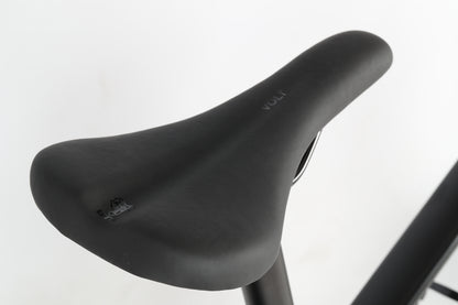 Close-up of a sleek, black bicycle seat with a smooth surface and VOLT inscribed near the back, securely mounted on a metal seat post. It complements the Suntour fork against a plain white background. From the PD2 27.5 by Haro MTB.