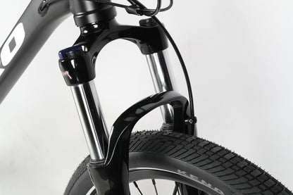 Close-up of a PD4 27.5 Haro MTBs black front fork with suspension and a Kenda tire, displaying shiny metal parts. The bike frame is partly visible against a white background, emphasizing its boost spacing for improved performance.