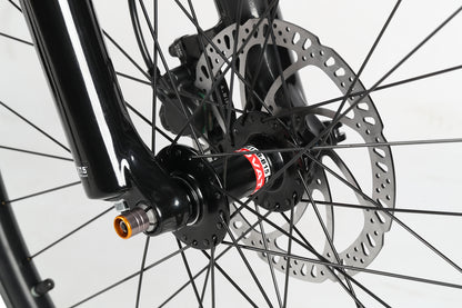 A close-up of the PD4 27.5 front wheel from Haro MTB shows a disc brake system with boost spacing. The metal rotor, attached to the hub among the spokes, is visible alongside a black fork displaying part of the PD4 logo and prominently features the disc brake mechanism.