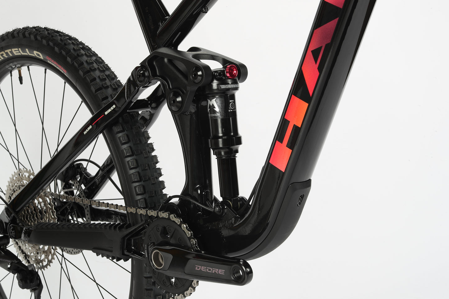 Close-up of a black Haro MTB Daley Alloy 2, an all-mountain 29er bike. It showcases the rear suspension system and drivetrain, red Daley logo on the aluminum frame, wide knobby tires, and detailed gear mechanism against a white background.