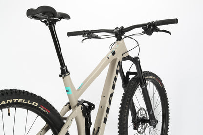 A close-up of the beige Haro MTB Daley Alloy 2 mountain bike with black handlebars and saddle highlights its aluminum frame. The bike is equipped with a suspension fork and knobby tires, ideal for off-road cycling. Standing against a white background, this all-mountain 29er is ready for adventure.