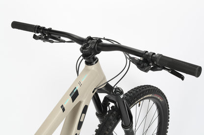 Close-up of the Daley Alloy 2 handlebar and front suspension by Haro MTB, showcasing a beige aluminum frame with black handlebars and rubber grips, set against a white background.