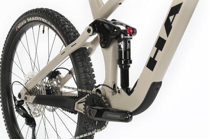 Close-up of a Haro MTB Daley Alloy 2 mountain bikes rear suspension and drivetrain, highlighting the Deore crankarm, rear shock absorber, and a portion of the rear tire with Vittoria Martello branding, showcasing its aluminum frame design and versatile all-mountain 29er features.