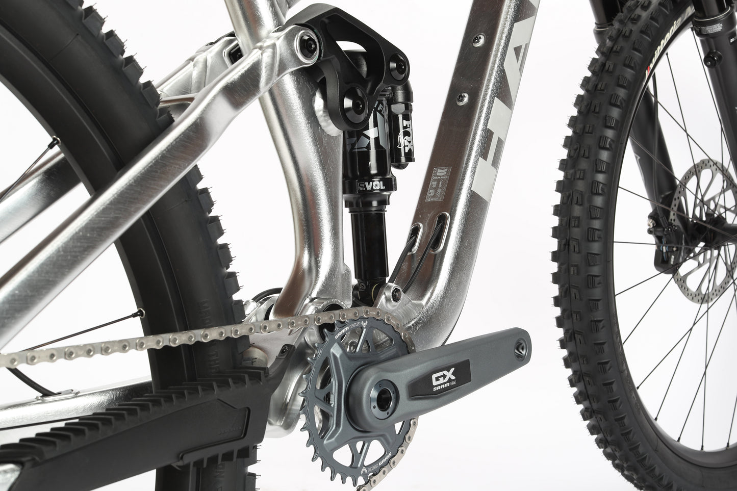 Close-up of the limited edition Daley Alloy LTD 1 mountain bike from Haro MTB reveals a silver metallic lower frame with GX crankset and suspension. Thick treaded tires and rear wheel showcase its rugged performance against a white background.