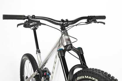 Close-up of a Haro MTB Daley Alloy LTD 1 mountain bike with a sleek silver frame. The image showcases the handlebars, suspension fork, and front wheels intricate tread against a white background, highlighting this limited edition models details and craftsmanship.