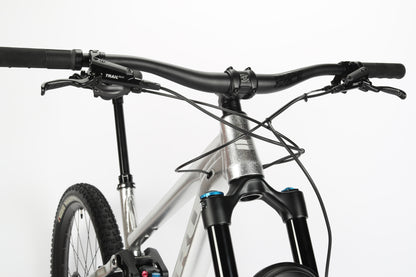 Close-up of the Haro MTB Daley Alloy LTD 2s front section highlights handlebars, brake levers, and a Fox suspension fork. The bike flaunts a silver frame with a minimalist design against a plain white background.