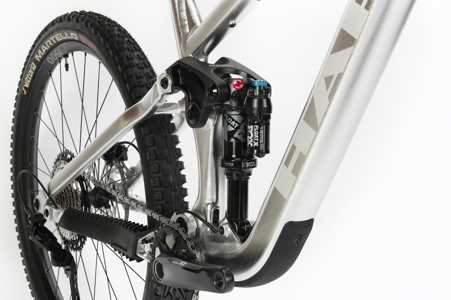 Close-up of a mountain bikes rear suspension and components features a Haro MTB Daley Alloy LTD 2 frame with Fox suspension, a black shock absorber, and a chainring. The partially visible tire showcases its tread pattern against a white background.