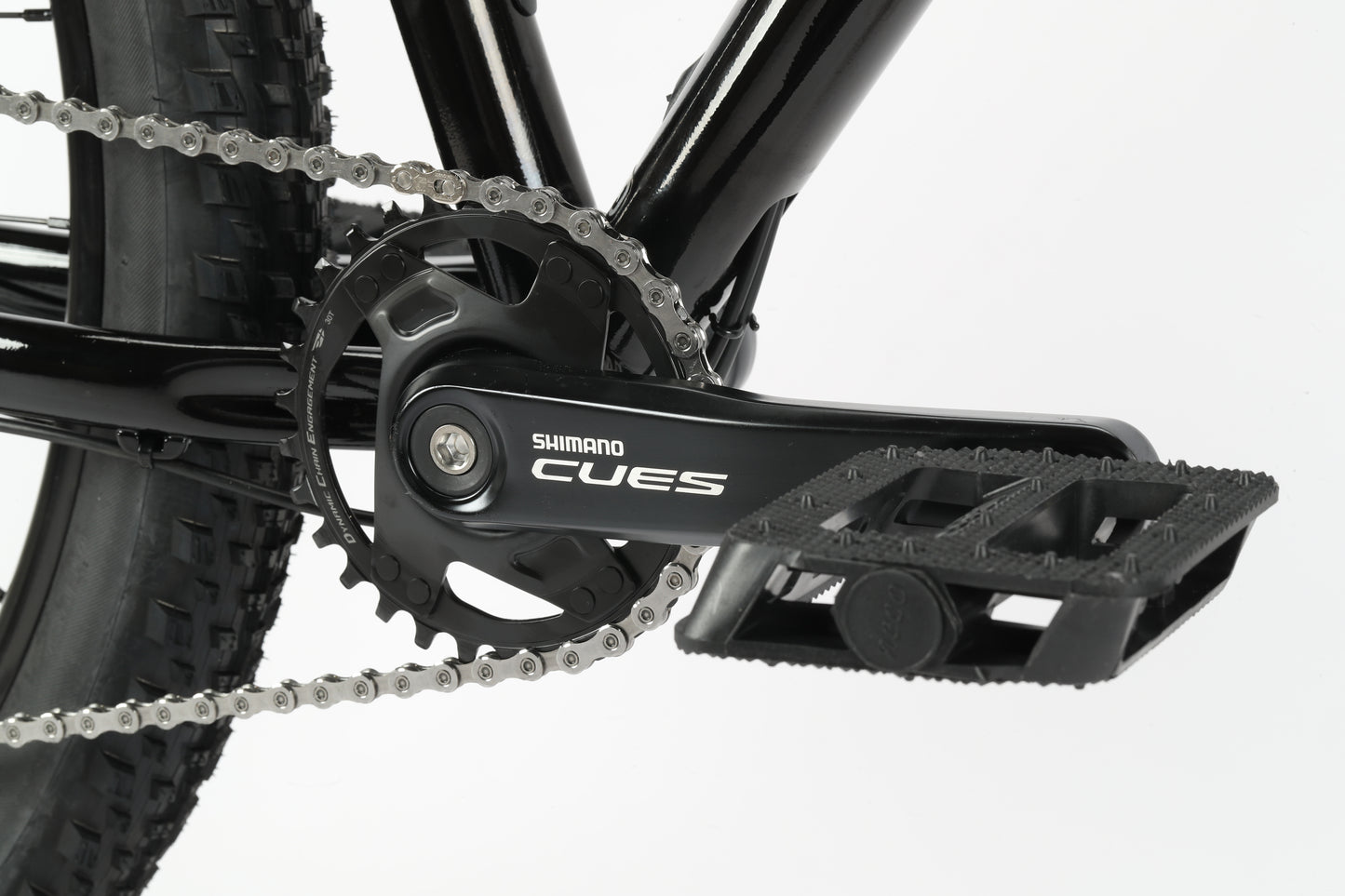 Close-up of a black Shimano CUES crankset on the Haro MTB Flightline LTD 29, showcasing chainring, chain, and pedal. The MTB frame peeks through, emphasizing the mechanical components designed for trail adventures.