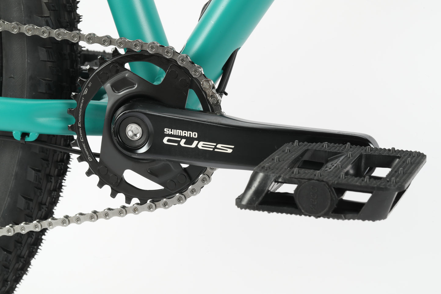 Close-up of a Haro MTB Flightline LTD 29s crankset and pedal with a teal frame, showcasing the Shimano Cues label on the crank arm. The chain is visible on the gear, with a textured black pedal surface and Tektro hydraulic brakes for superior control.