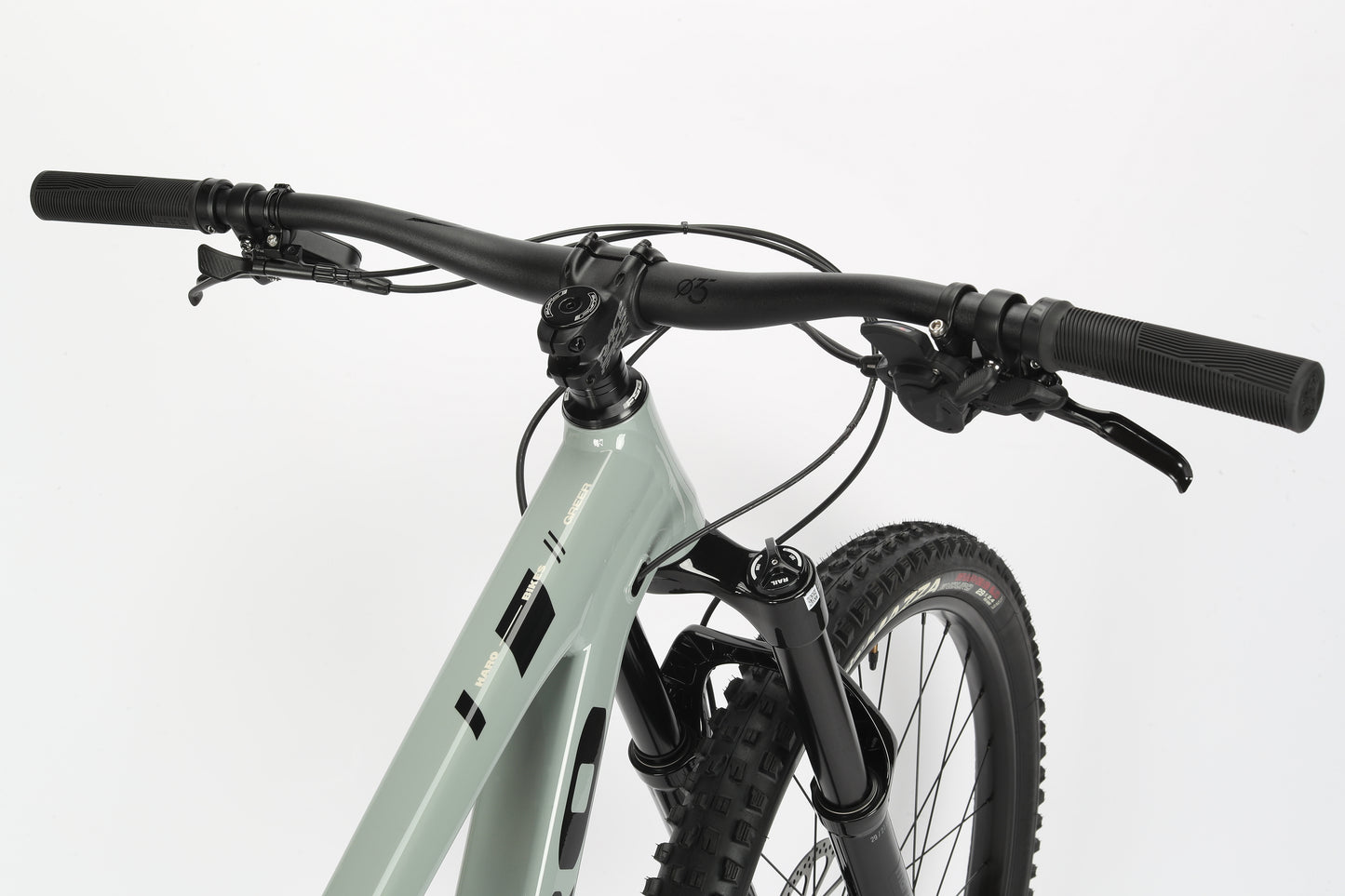 Close-up of a mountain bikes handlebars and front suspension features the sleek Haro MTB Greer Alloy 2 with a matte gray performance alloy frame; lever-style brakes complete the design against a white background.