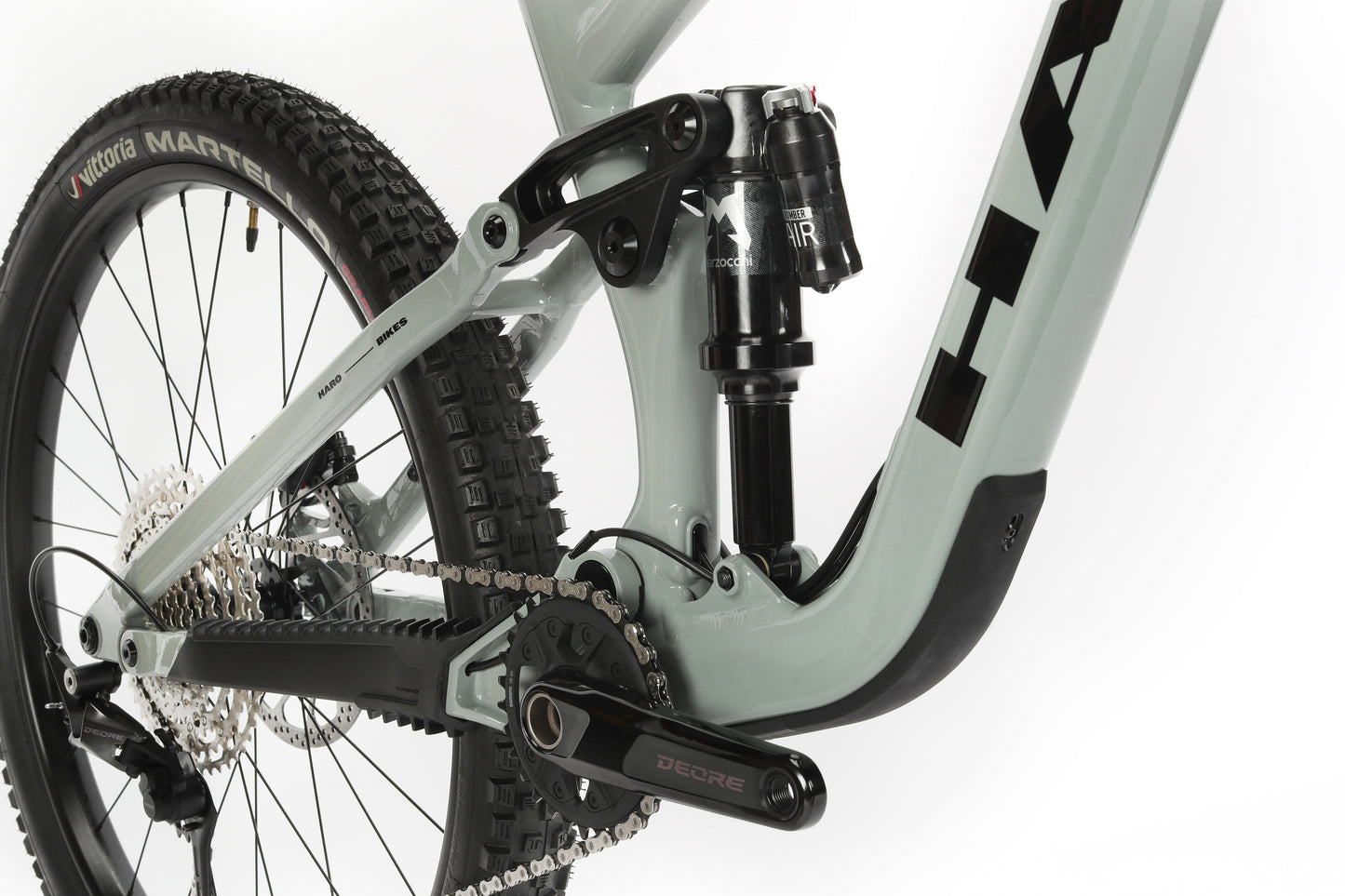 A close-up of the Greer Alloy 2 by Haro MTB showcases its rear suspension and drivetrain, including the chainring, pedals, shock absorber, and tire. The performance alloy frame boosts strength and agility while highlighting the bikes technical features and mullet wheel setup.