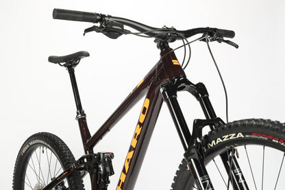 The Greer Alloy 2, a mountain bike by Haro MTB, showcases a black performance alloy frame with orange accents. It features dual suspension, thick tires, a Shimano gear set, and mullet wheel configuration. The steering handlebars and front fork stand out against the plain white background.