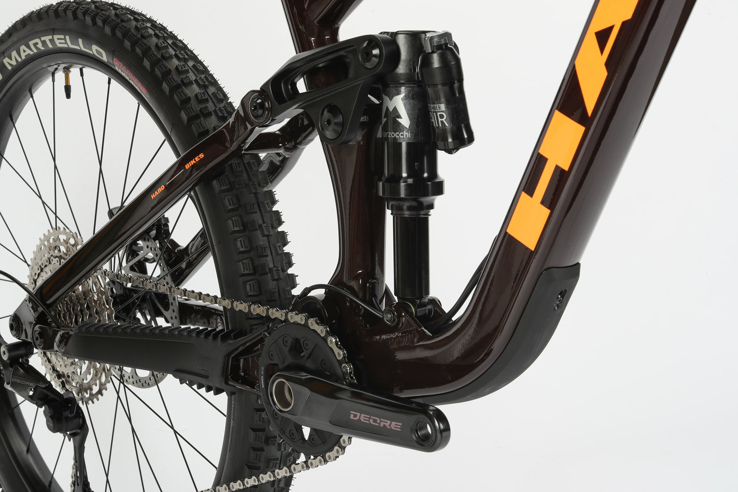 The Greer Alloy 2 by Haro MTB showcases a close-up of its rear suspension and drivetrain, featuring a dark frame, shock absorber, and detailed chain mechanism with Deore branding. It has a mullet wheel setup for improved handling against a plain white background.