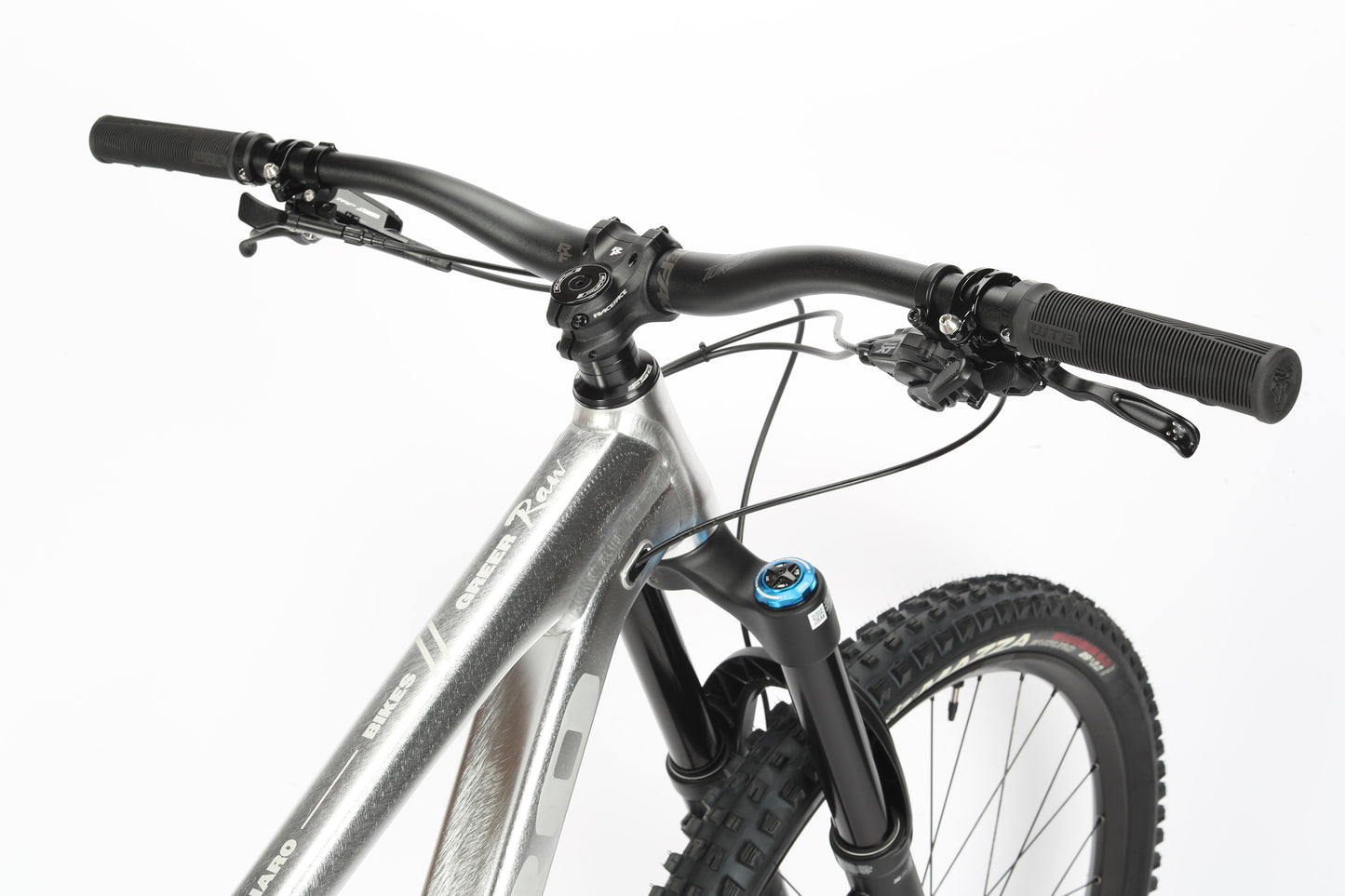 Close-up of the Greer Alloy LTD 2 by Haro MTB, showcasing its sleek aluminum frame, Fox suspension, handlebars, and front tire. The gray mountain bike features black grips and gear shifters against a plain white background.