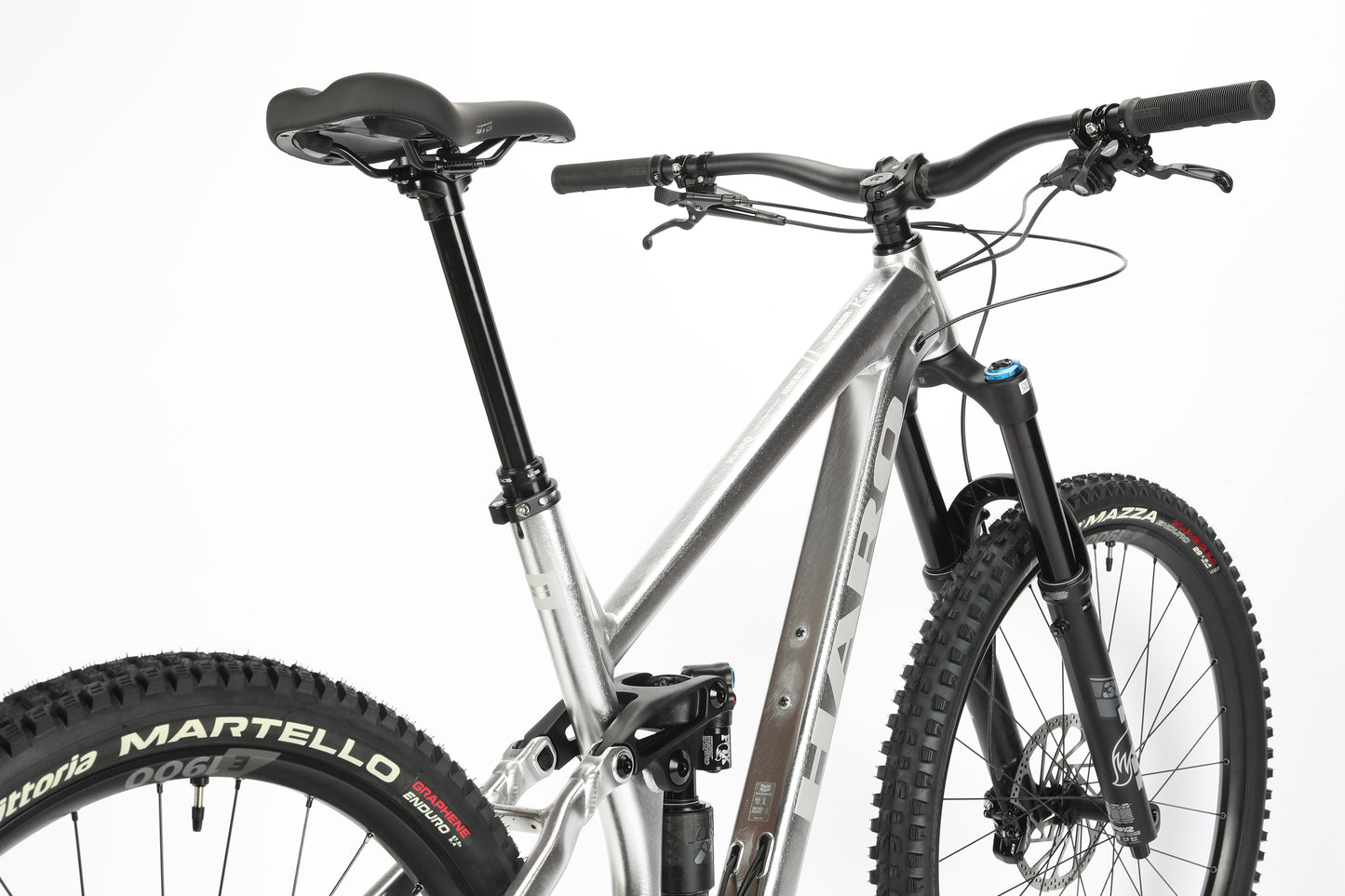 A close-up of a Haro MTB Greer Alloy LTD 2 mountain bike features its aluminum frame and front Fox suspension, with wide knobby Vittoria tires. It has a black seat post, handlebars, grips, and front disc brakes set against a white background.