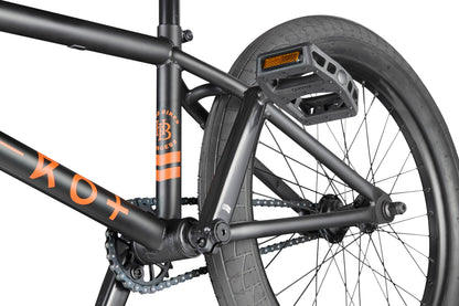 Close-up of the Burgess BMX bike frame, pedal, rear wheel, and chain with orange accents—perfect for advanced riding.