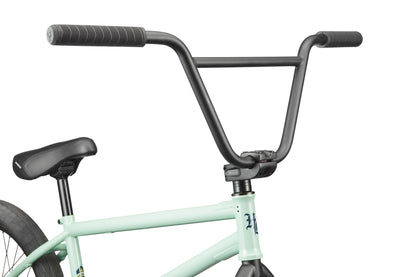 Close-up of the Burgess BMX bike’s handlebars, seat, and frame; its light green body and black handlebars stand out.