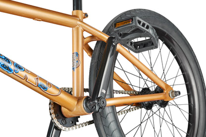 Close-up of the Dana's rear wheel, pedals, and chain—bronze BMX bike with black tires, blue graphics, pro-level street performance.