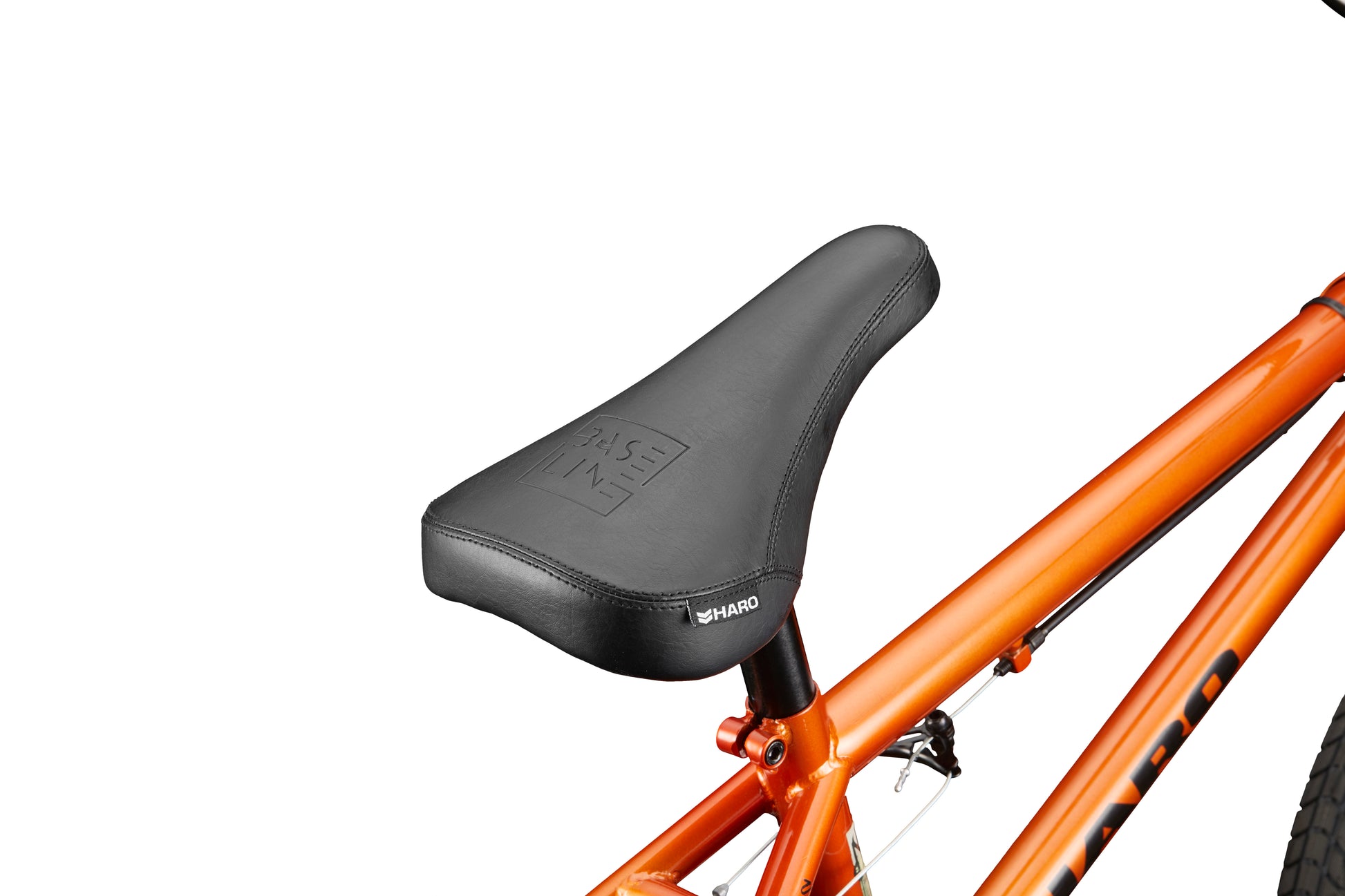 Close-up of the Downtown 16's black BMX seat on an orange frame, ideal for young riders, shown against a white background.