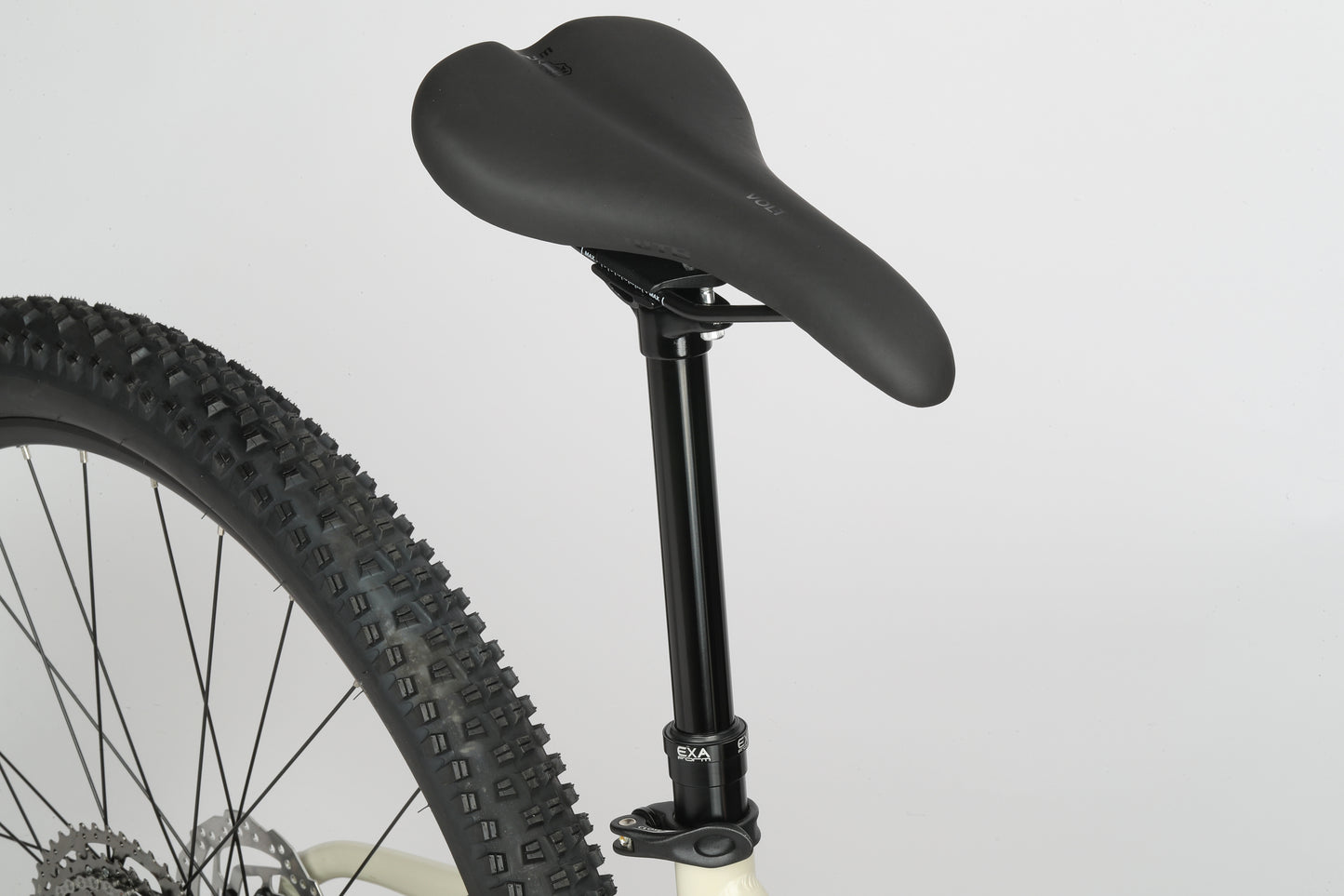 Close-up of the black seat on a Double Peak 1 bike with a large knobby tire, set against a white background.