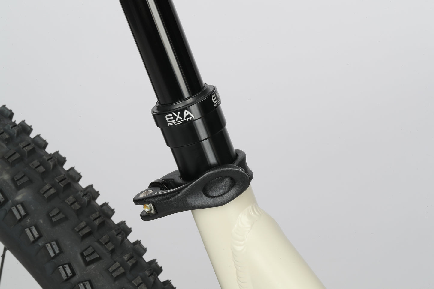 Close-up of Double Peak 1 showing a Shimano Cues drivetrain, knobby tire, white frame, and black EXA Form clamp on the seat post.