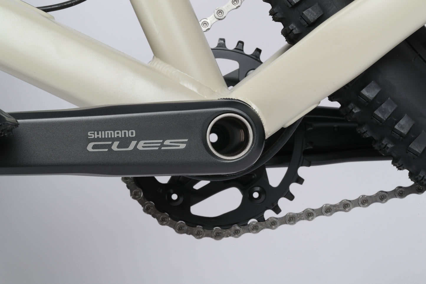 Close-up of a Shimano CUES crankset and chainring on a Double Peak 1 beige frame, with a black tire in the background.