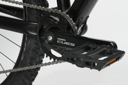 Close-up of a black crankset and pedal with a chain, showcasing the Shimano Cues logo on Double Peak 2.